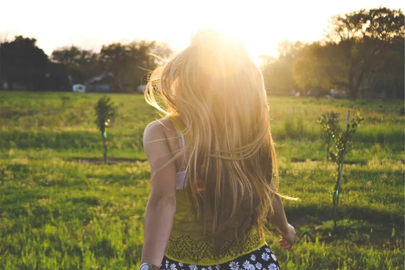 Mulher caminhando num gramado contra o sol